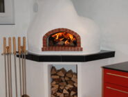Ein weisser Pizzaofen in einer Küche, es wurde eingefeuert und das Holz brennt.